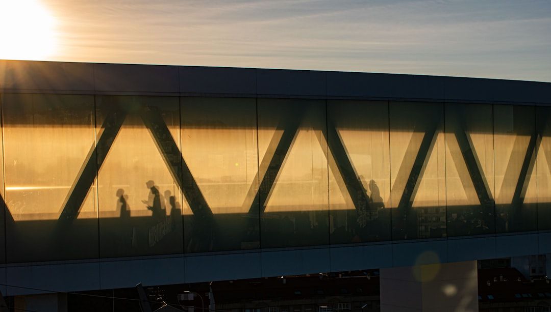 Silhouetted people walk through a modern glass bridge at sunset