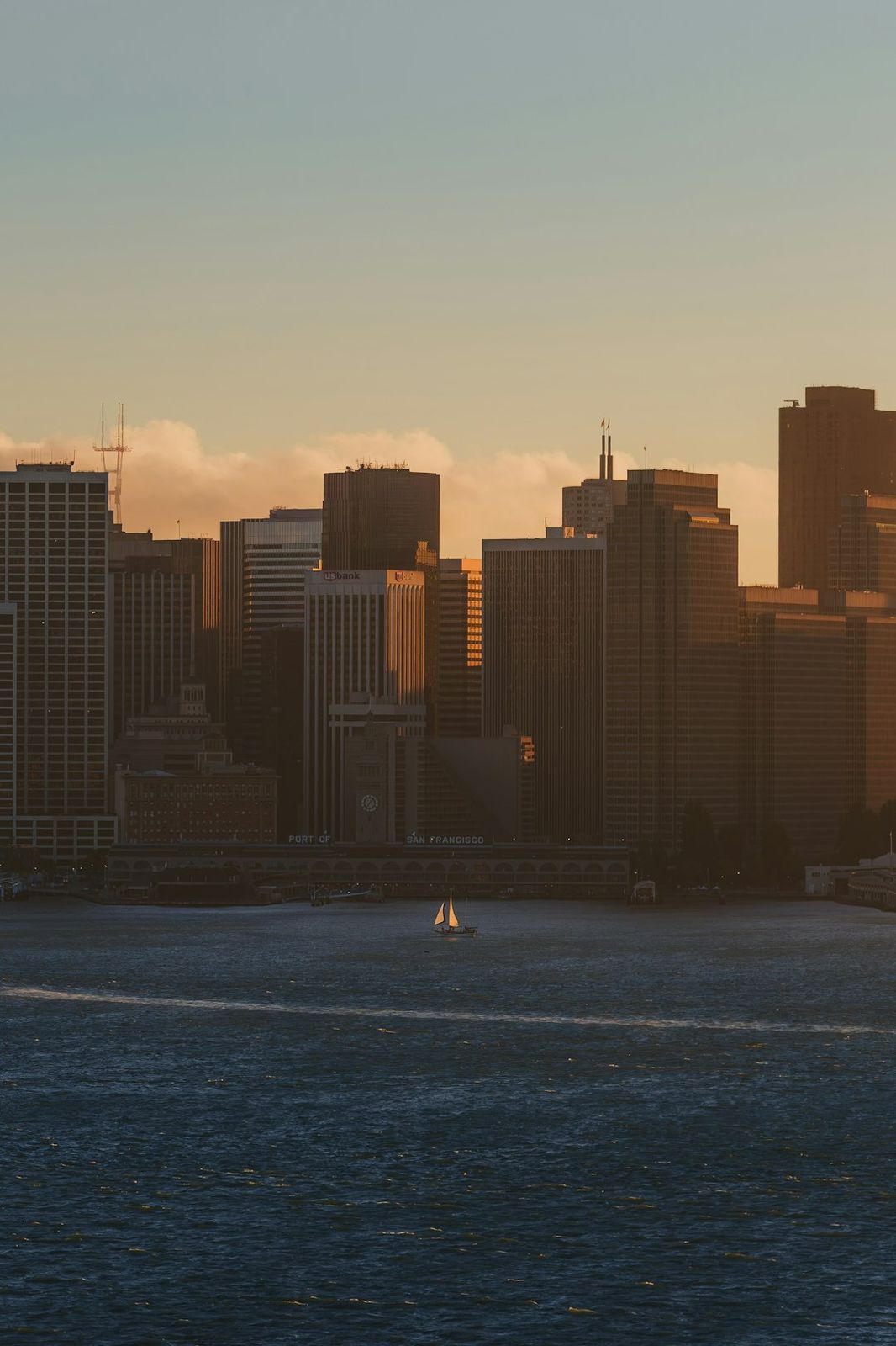 A sailboat on the bay before the San Francisco skyline at golden hour