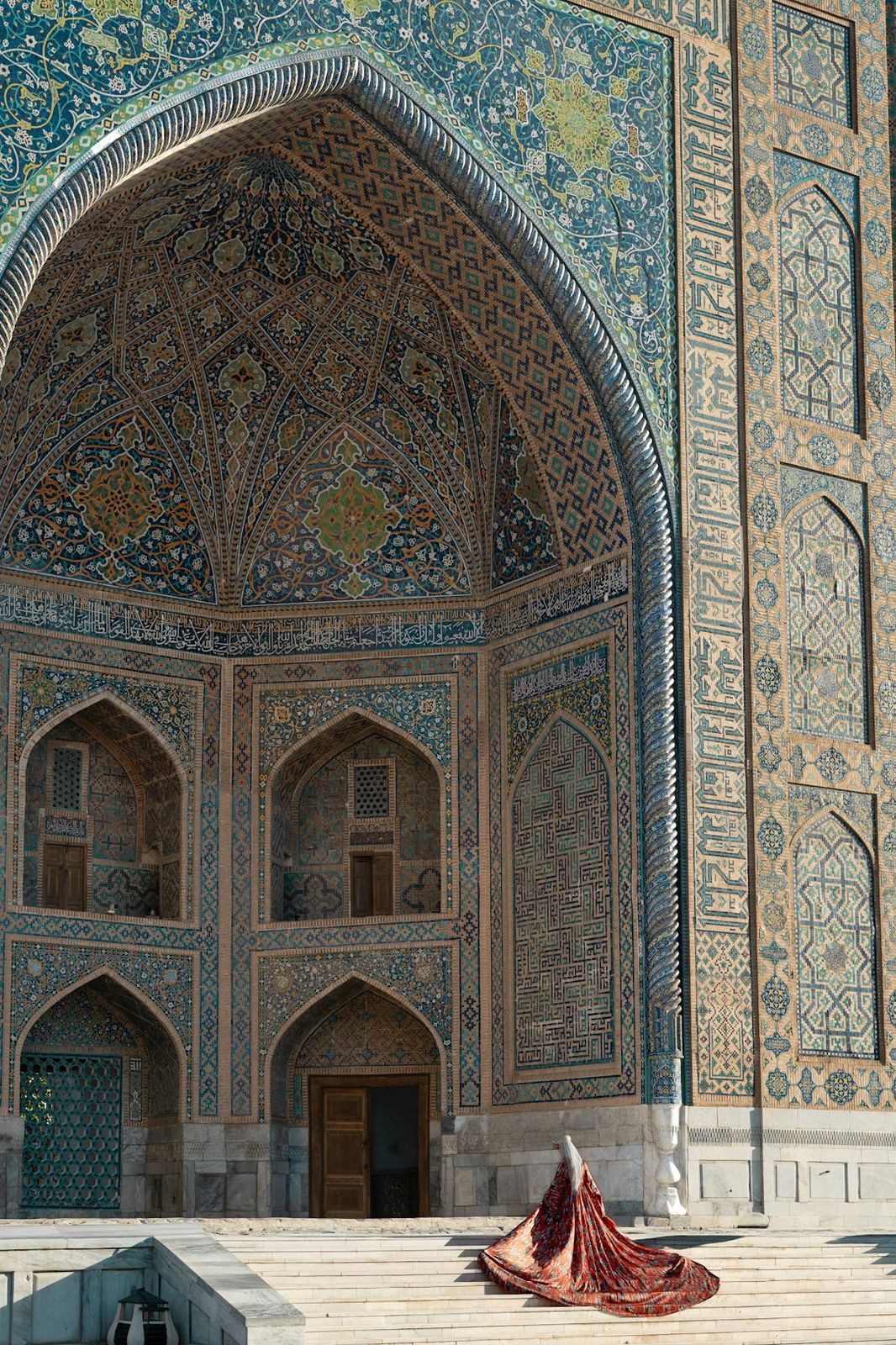 A person in a red dress before a tiled archway in Samarkand
