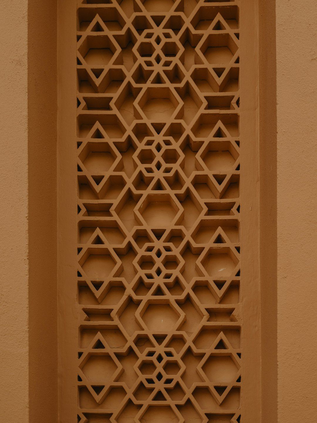 A carved geometric lattice screen with star patterns in warm sandstone at Masjid Tengku Ampuan
