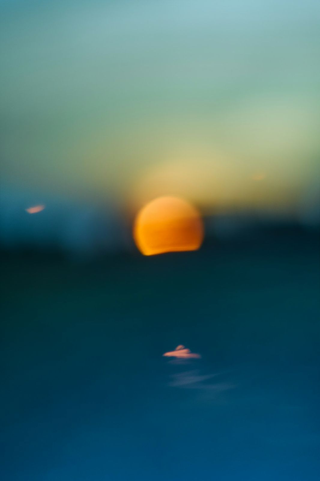 A blurred orange orb of low sun reflecting on dark blue water