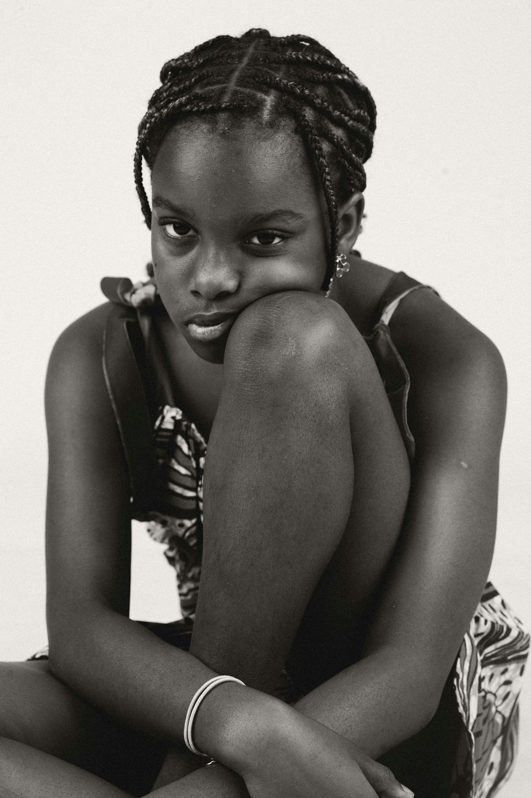 A young girl with braided hair resting her chin on her knee