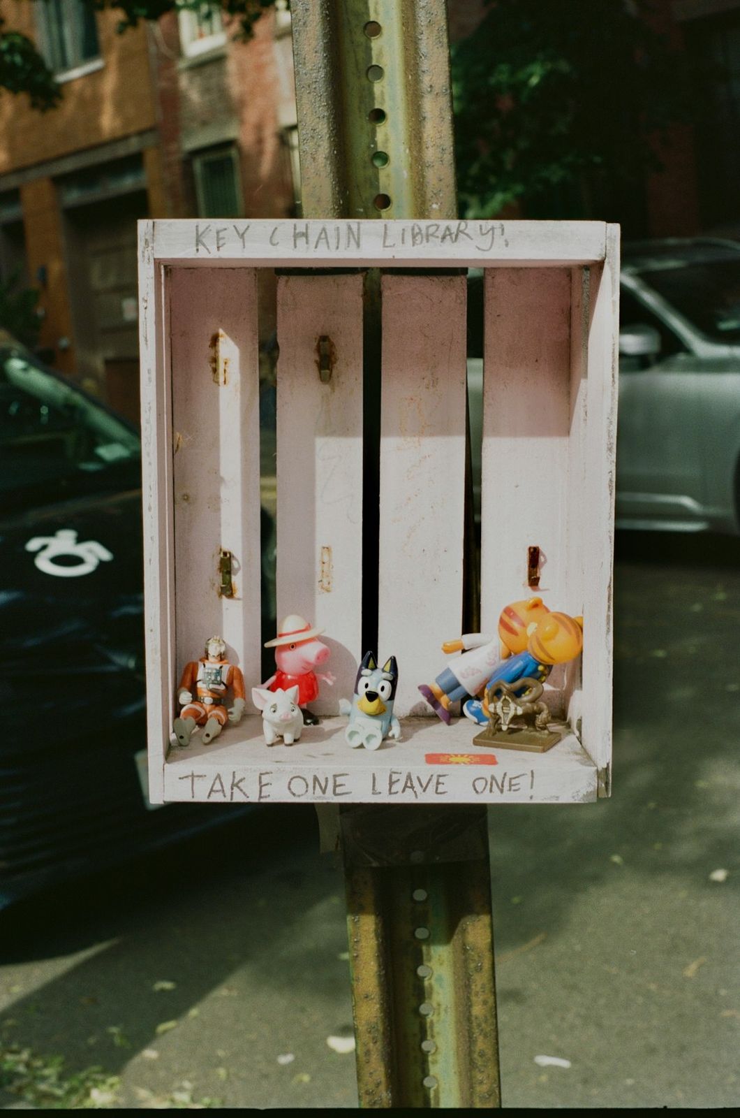 Small plastic figurines inside a wooden box labeled Key Chain Library on a post