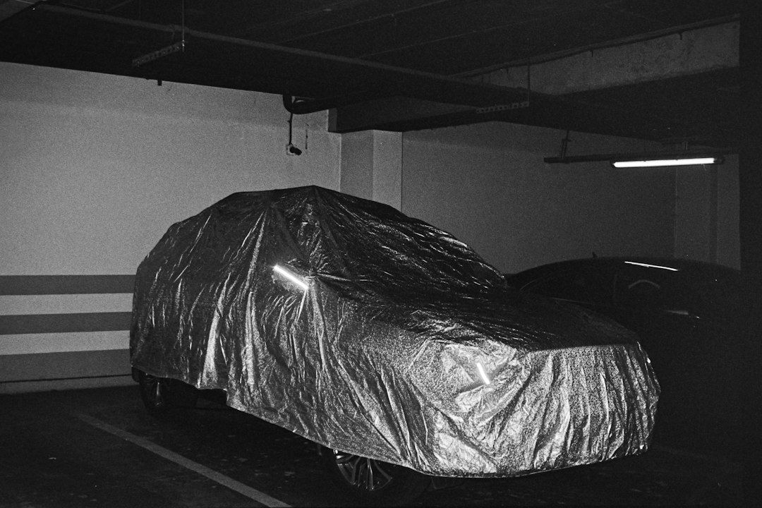 A car covered in a reflective silver tarp parked in a dim concrete parking garage