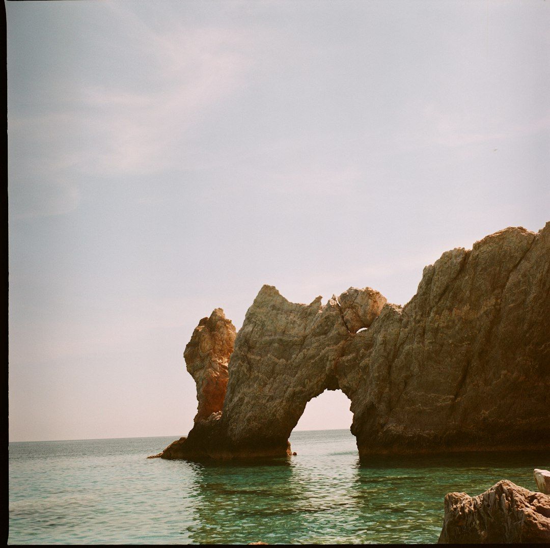 A natural stone arch rising from clear turquoise water under a pale sky