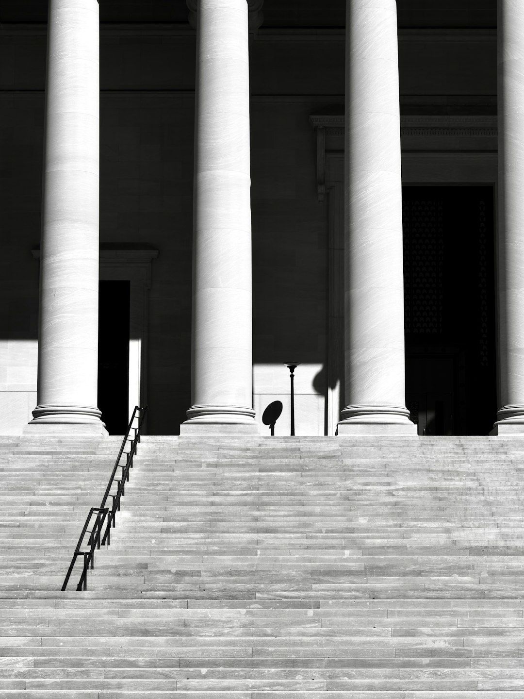 Stone columns and stairs leading to a dark entrance in black and white