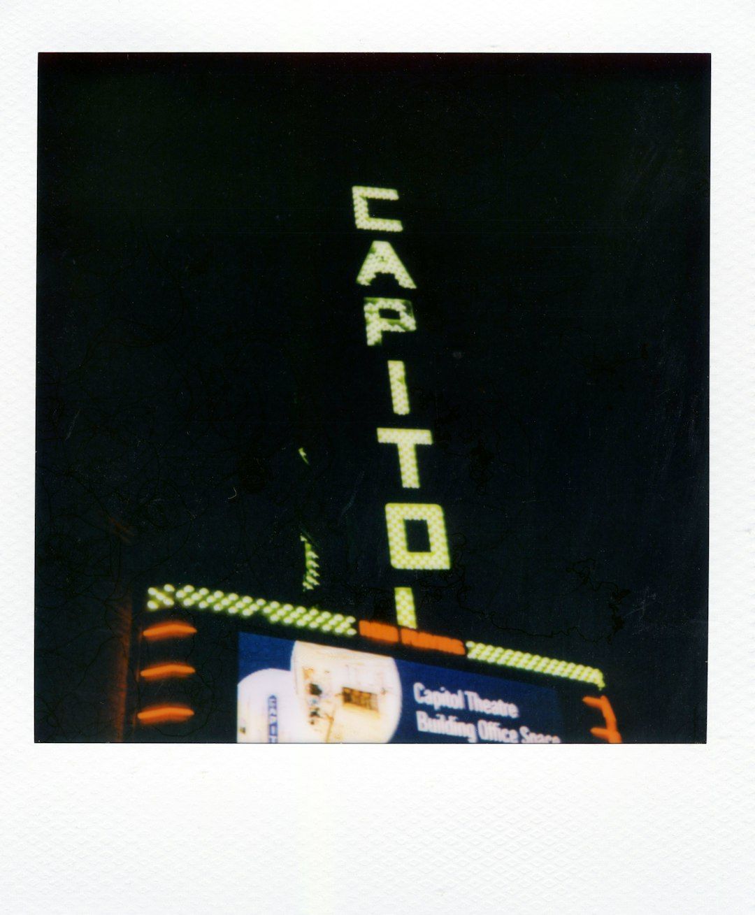 A vertical neon sign reading CAPITOL above a theatre building at night