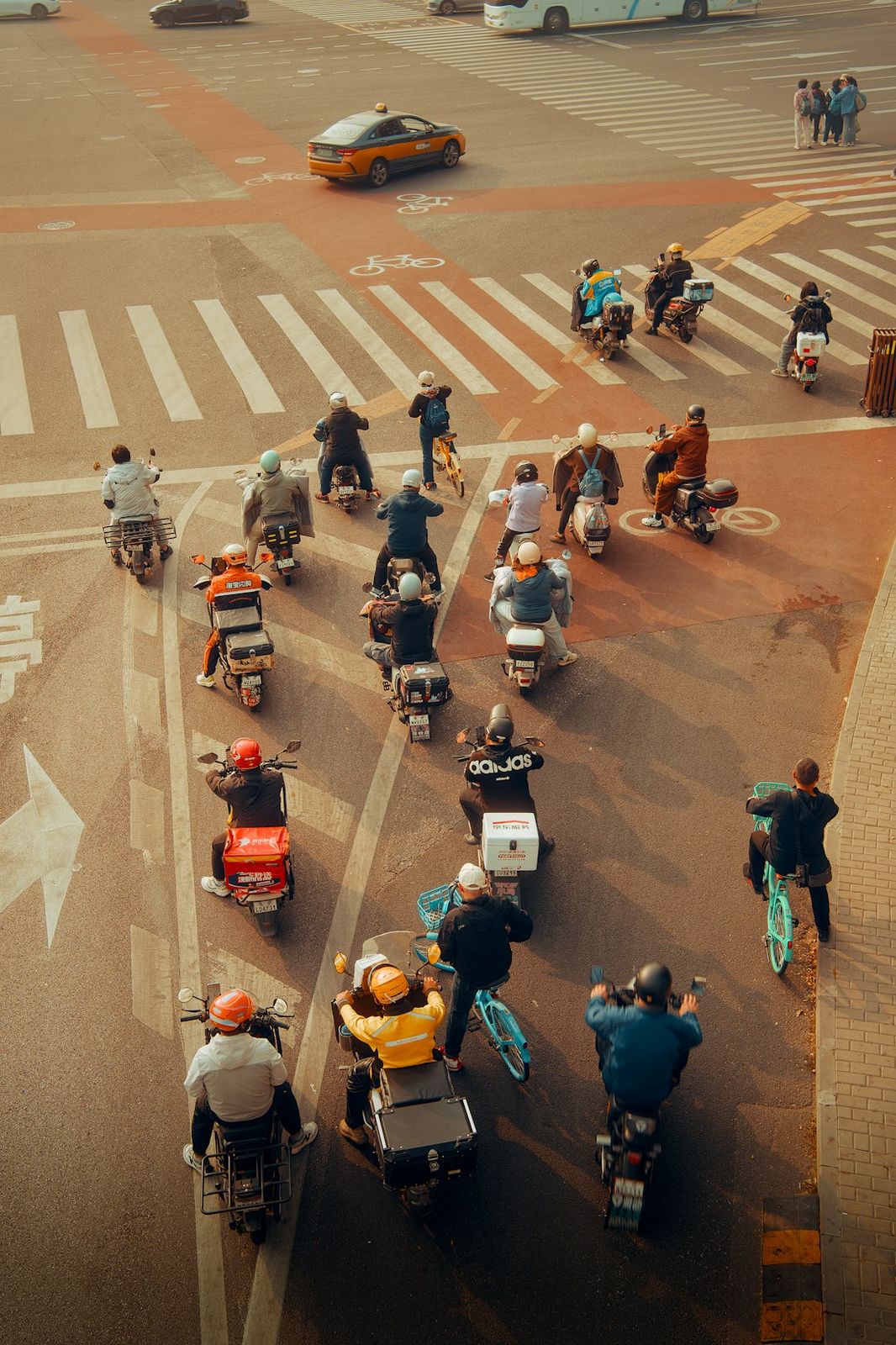 A group of people on scooters and bicycles waiting at a city intersection in warm light