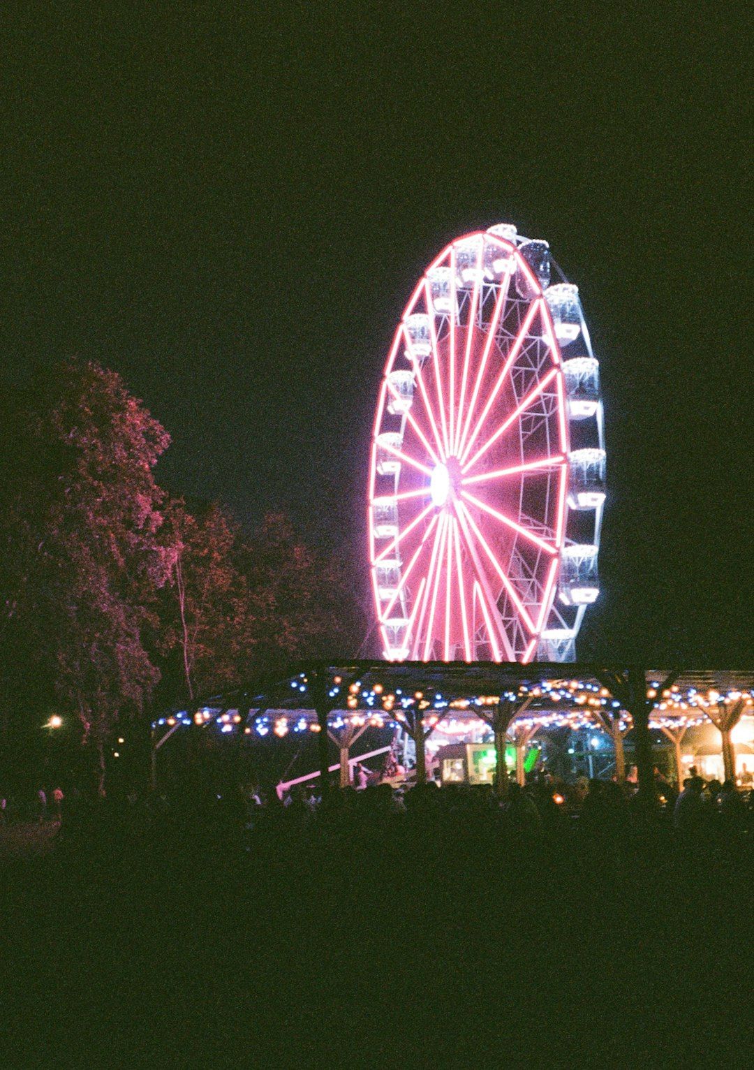 A glowing red ferris wheel at night above a canopy of string lights in Budapest