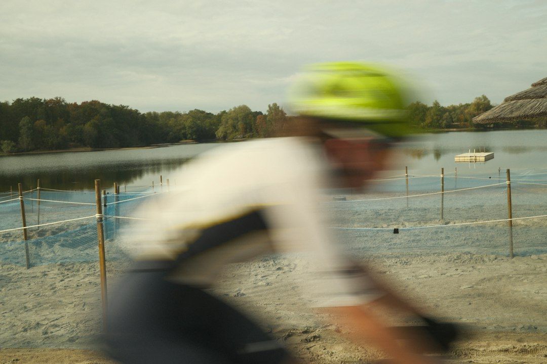 A cyclist in a bright helmet riding past a sandy beach and lake