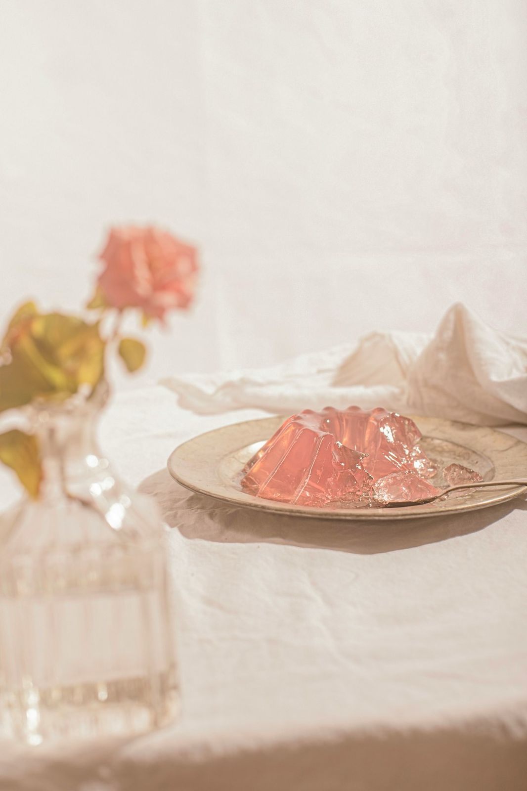 A pink gelatin dessert on a metal plate with a rose in a vase