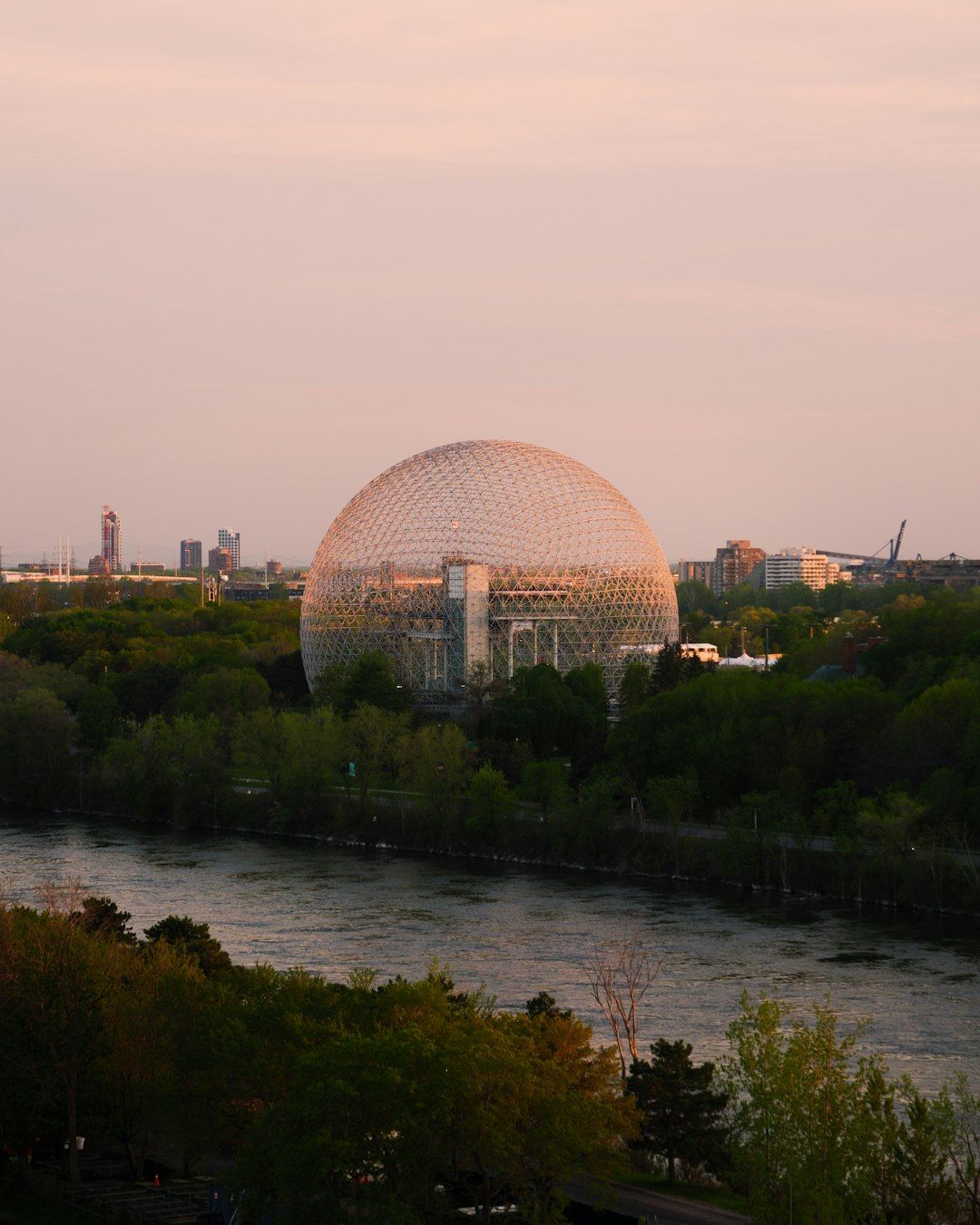 A large geodesic dome building by a river at sunset