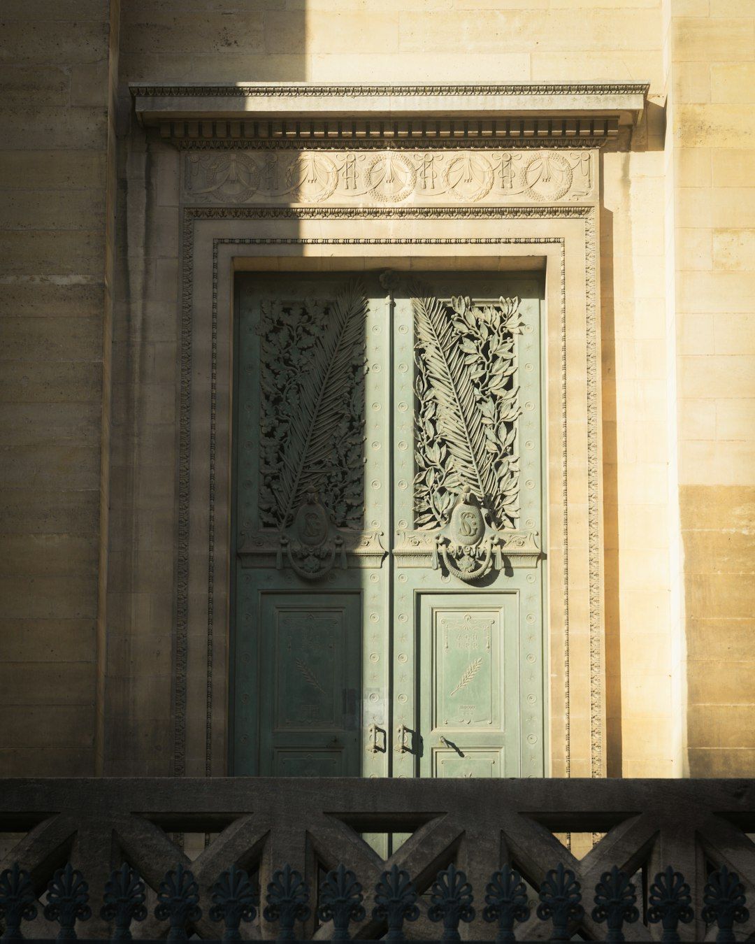 Ornate green double doors with carved palm leaves in a stone building facade