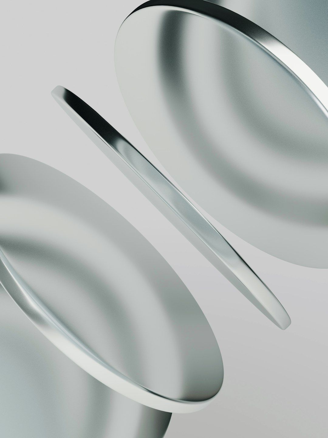 Three smooth metallic discs floating at an angle against a light grey background