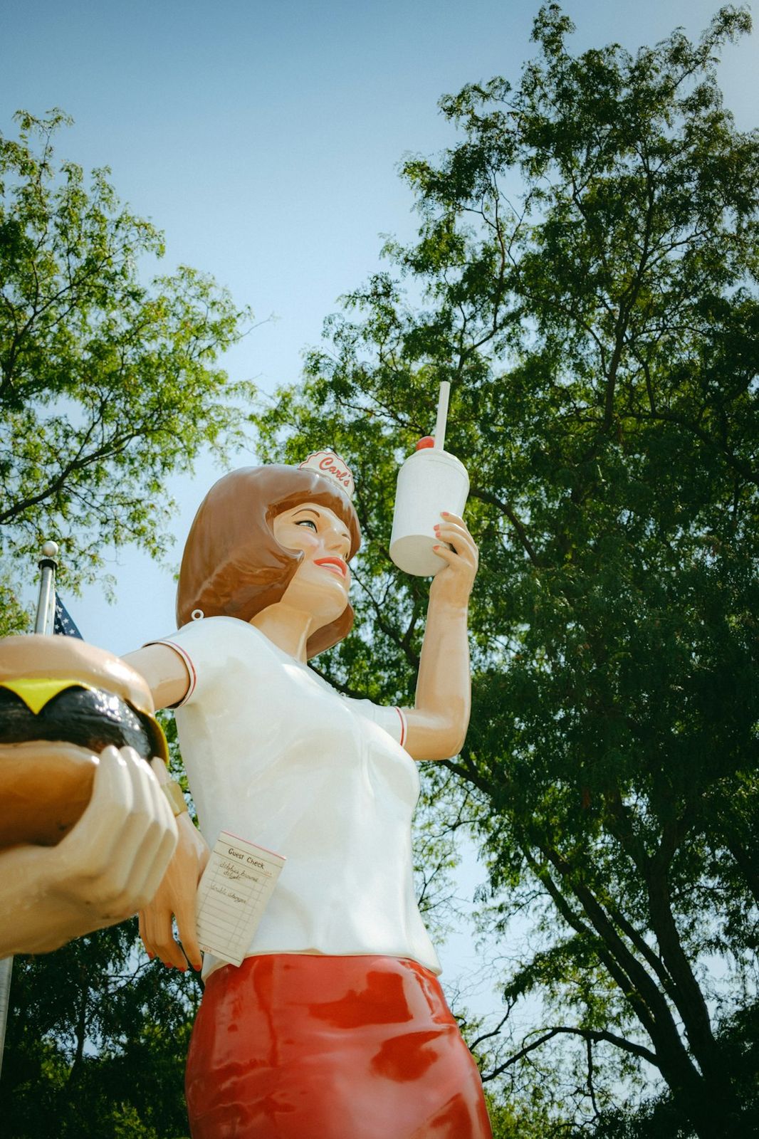 A fiberglass statue of a woman holding a burger and a drink outdoors