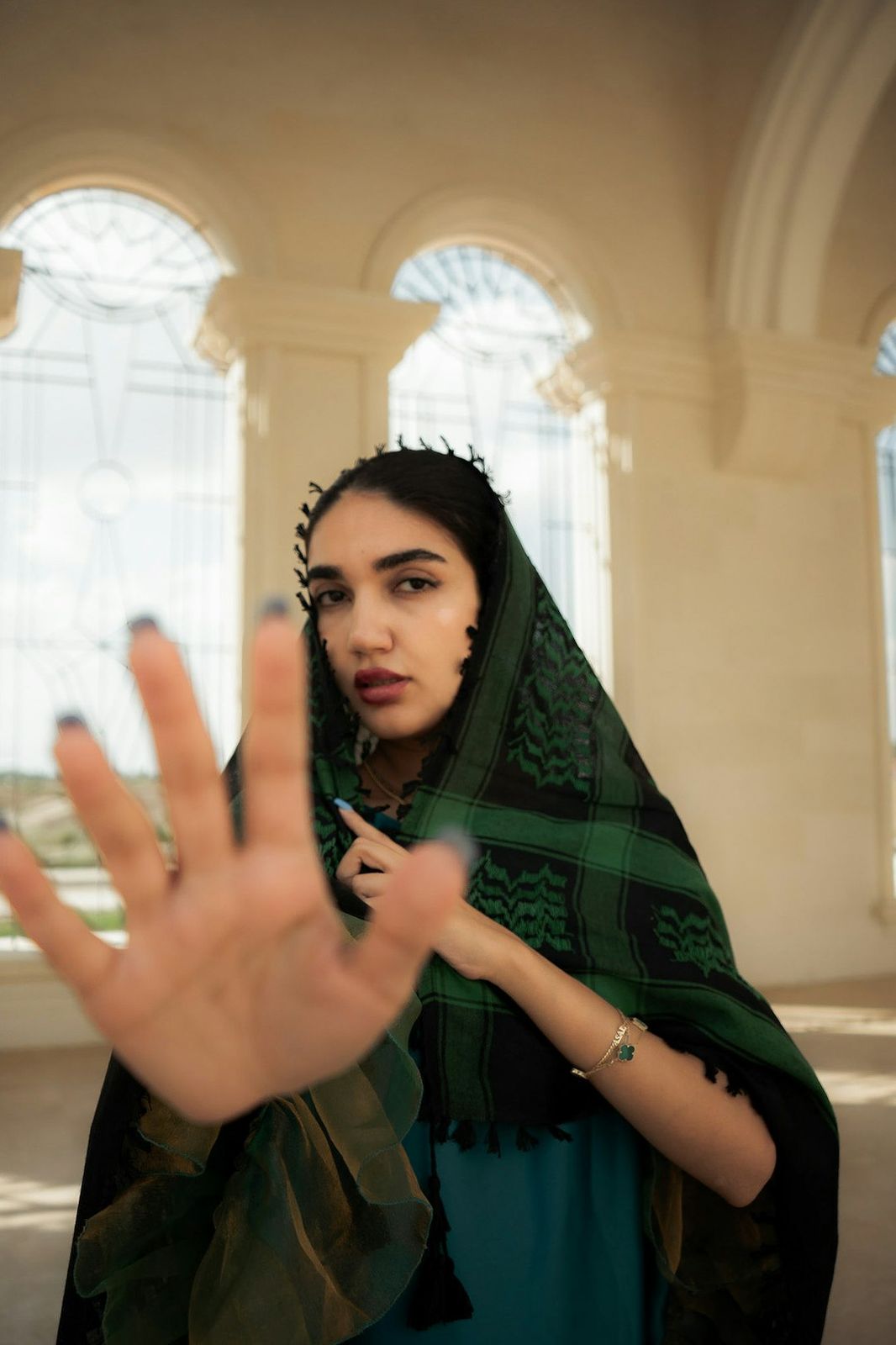 A woman with a green and black patterned headscarf holding her hand out in a gesture